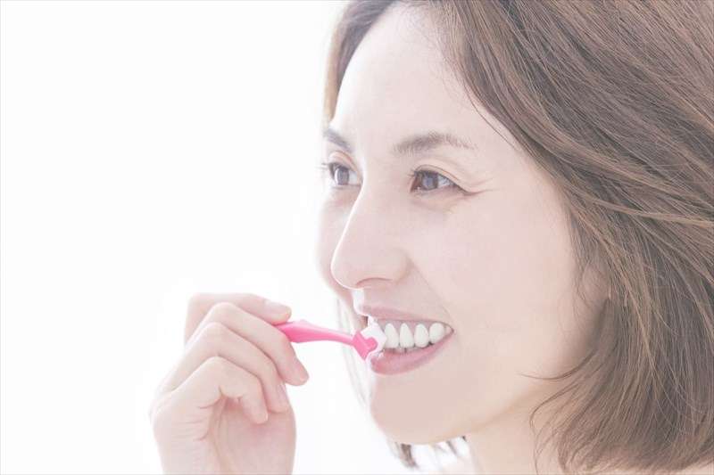 ピンク色の歯ブラシで歯を磨いている女性